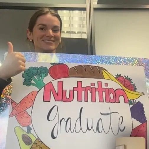 Fitness program graduate at Relentless Athletics holding a Nutrition Graduate sign